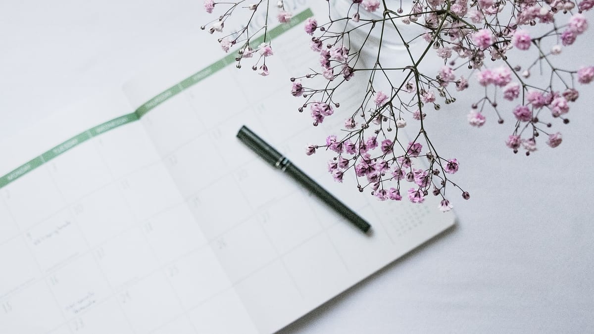 Agenda mensuel ouvert sur une table blanche avec un stylo noir, à côté d'un bouquet de gypsophile rose